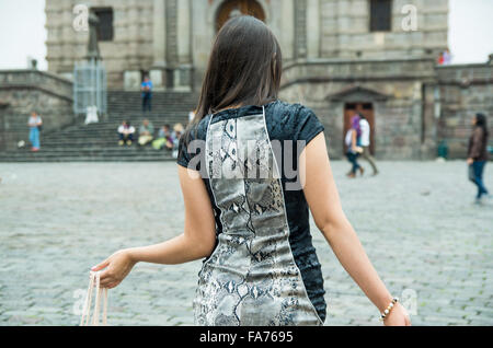 Brunette classy woman back facing camera walking across city plaza carrying shopping bags. Stock Photo