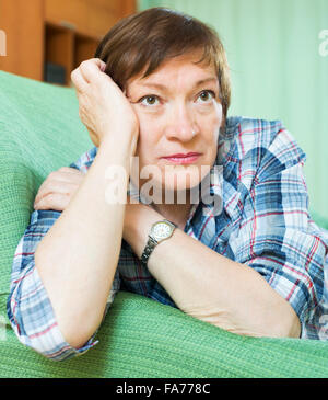 Stressed elderly female laying on her elbows and thinking  on couch Stock Photo