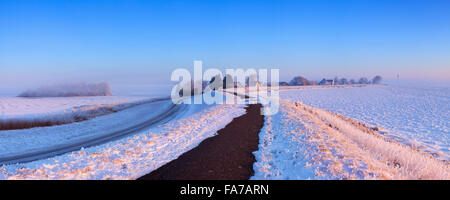 Sunrise over a dike along a frozen lake on a record-breaking cold morning near Uitdam in The Netherlands. Stock Photo