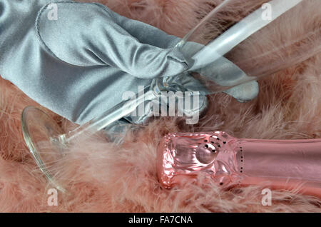 Pink champagne bottleneck and a lady's hand in silver glove holding wine glass on pink marabou feather Stock Photo
