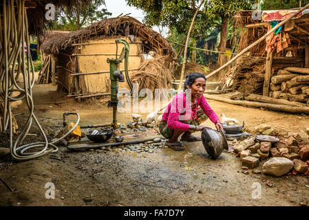 Old nepalese woman washes dishes with water from a well outside Stock Photo