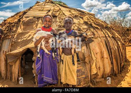 Two girls from the African tribe Daasanach holding goats in front of their home Stock Photo