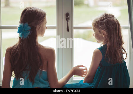 Two cute sisters looking behind the window Stock Photo