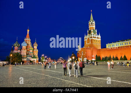 Tourists walk in the Red Square near the Spasskaya Tower and the Saint Basil's Cathedral brightly illuminated at night. Moscow, Russia. Stock Photo