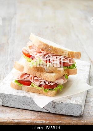 Stack of wafer thin ham sandwiches on sliced white bread with salad leaves and tomatoes Stock Photo