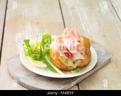 Wafer thin ham in baked potato with salad leaves and spring onions on white plate and whitewashed cutting board Stock Photo