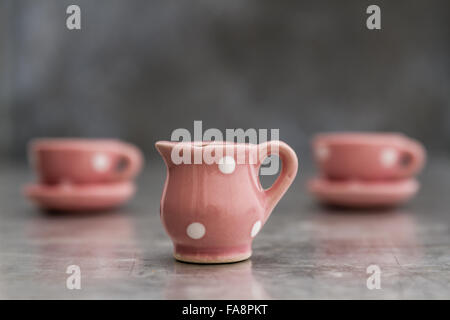 Little pink toy porcelain cups and plates with white dots on gray background Stock Photo