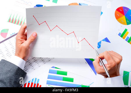 closeup of a young caucasian businessman at his office desk full of graphs and charts observing a chart with a downward trend Stock Photo