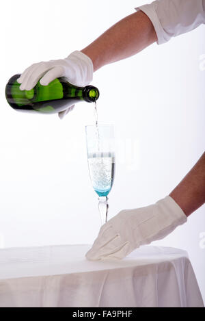 Waitress wearing white cotton gloves pouring sparkling wine from a green bottle Stock Photo