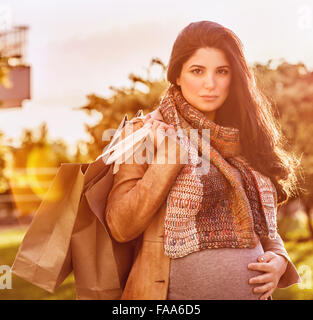Portrait of beautiful pregnant woman with shopping bag outdoors in sunny day, happy shopping in pregnancy period Stock Photo