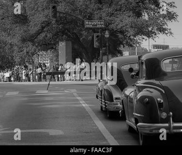 Extras and vehicles on set awaiting the presidential motorcade in front of the Texas School Book Depository in Dallas, Texas. Stock Photo