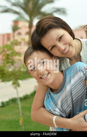Smiling mom and teen son hugging with large plants in background Stock