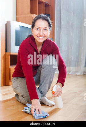 mature woman polishing parquet floor with furniture polish at home Stock Photo