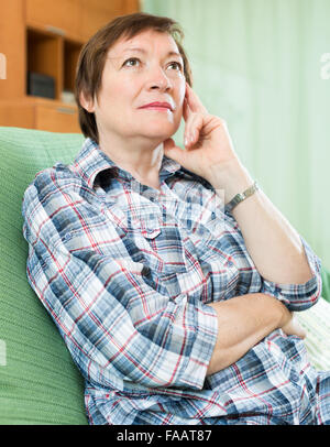 Stressed female pensioner laying on her elbows and thinking indoor Stock Photo