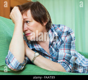 Stressed elderly woman laying on her elbows and thinking indoor Stock Photo