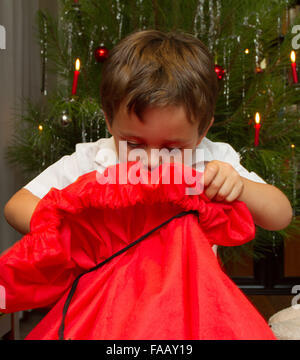 Young boy opening christmas present in front of tree with candles. Stock Photo