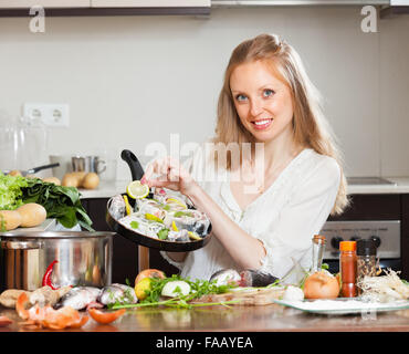 Smiling girl cooking fish with lemon in frying pan at home Stock Photo