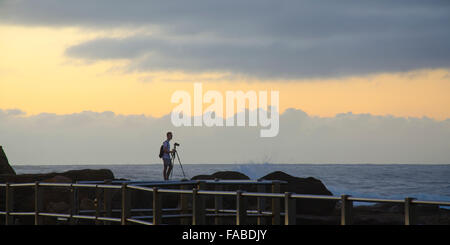 A lone photographer stands on the rocky coastline while capturing the morning light at a Sydney beach in Australia