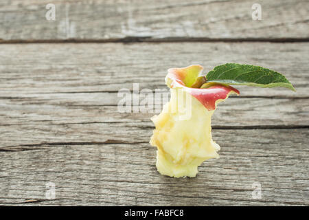 Bitten into apple core with green leaf on rustic wood Stock Photo
