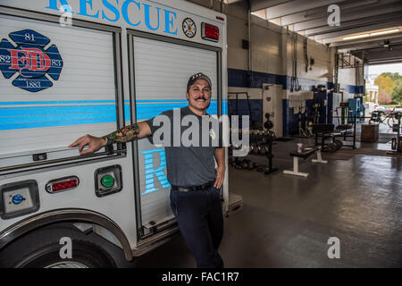 Florida fire fighter with arm tattoos and  mustache posing in fire station in front of a rescue vehicle wearing fire department T shirt and cap. Stock Photo