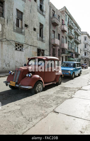 A red vintage automobile parked along a stone curb on a street in Havana Cuba with a newer blue car parked behind it. Stock Photo