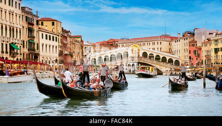 Tourists in gondola exploring Grand Canal, Rialto Bridge in the background, Venice, Italy