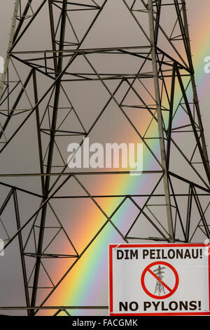 A rainbow over electricity pylons leaving Wylfa nuclear power station on Anglesey, Wales, UK, with a portest sign. Stock Photo