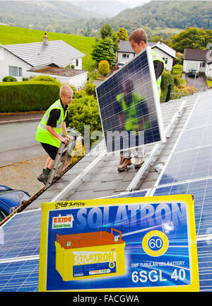 Technicians fitting solar photo voltaic panels to my house roof in Ambleside, Cumbria. Although the Lake District is renowned for its wet, cloudy climate, with Ambleside receiving some 70 inches of rain annually, these panels generate three quarters of my electricity needs. Composite image with a solar battery. Stock Photo