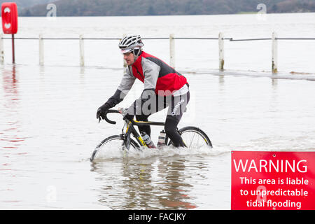 A cyclist travels through flood waters on the road at Storth on the Kent Estuary in Cumbria, UK, during the January 2014 storm s Stock Photo