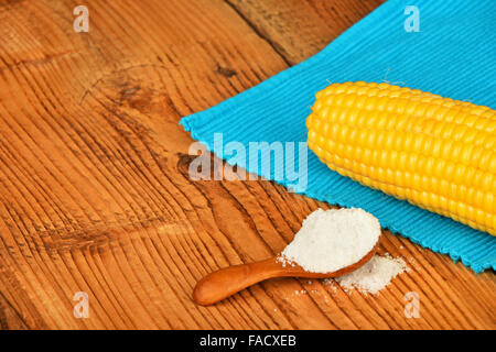 One open fresh yellow corn cob and salt in scoop with blue cloth napkin on brown vintage wooden surface Stock Photo