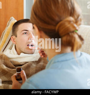 caring woman giving cough syrup to unwell man at home Stock Photo