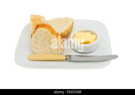 Crusty bread with butter in a ramekin and a knife on a plate isolated against white Stock Photo