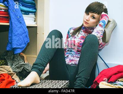 Portrait of a beautiful young woman sitting surrounded by scattered clothes Stock Photo