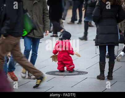 A boy dressed in a warm red one-piece suit stands between pedestrians on Zeil shopping street in Frankfurt am Main, Germany, 28 December 2015. Photo: FRANK RUMPENHORST/dpa Stock Photo