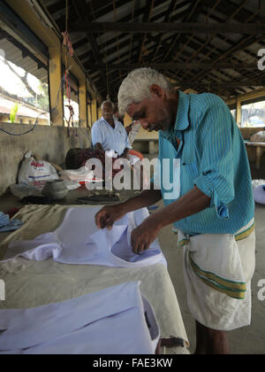 Laundry  worker concentrates on folding a white laundered white shirt - Kochi Community Laundry India Stock Photo