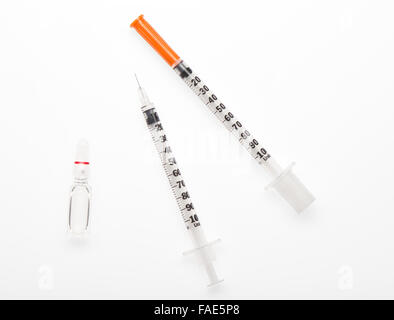 Plastic syringe with needle closed by protective cap, plastic syringe with open needle and transparent white glass ampoule Stock Photo