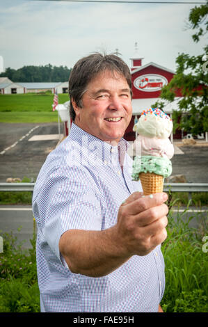 Man holding a three scooped ice cream cone in front of his creamery