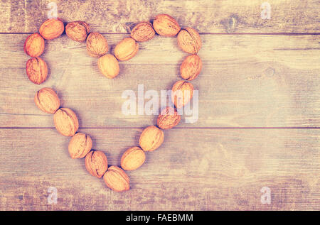 Vintage toned heart made of walnuts on wooden background, space for text. Stock Photo