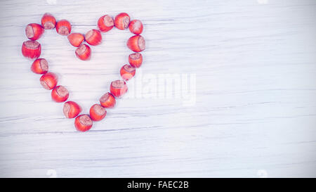 Vintage toned heart made of hazelnuts on wooden background, space for text. Stock Photo