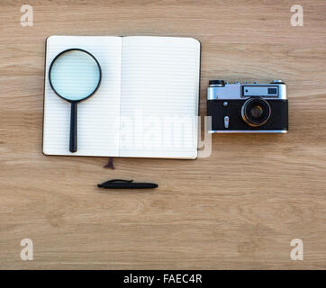 Open Notepad, pen, magnifying glass and camera on the table top view. Stock Photo