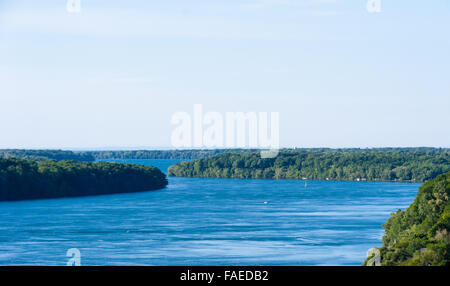 Large wide river winding through forested area under white empty sky. Stock Photo