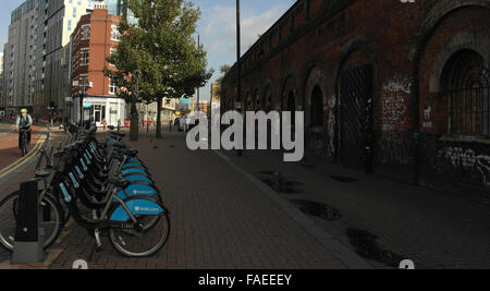 Barclays cycle hire docking station by old railway wall with graffiti scrawl, Bethnal Green Road to Sclater Street, London, UK Stock Photo