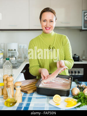 Smiling woman preparing slices of white fish for baking Stock Photo