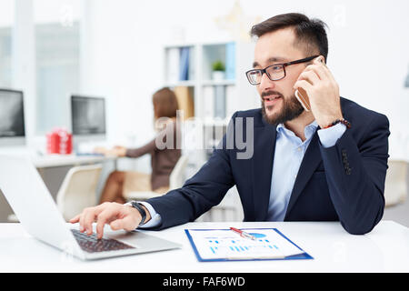 Confident businessman typing on laptop and speaking on the phone Stock Photo
