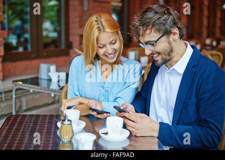 Smiling young couple using smartphones at cafe Stock Photo
