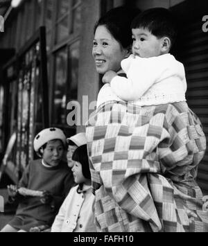 Eine Mutter trägt ihr Kind durch die Straßen von Kyoto, Japan 1960er Jahre. A mother carrying her baby through the streets of Kyoto, Japan 1960s. Stock Photo