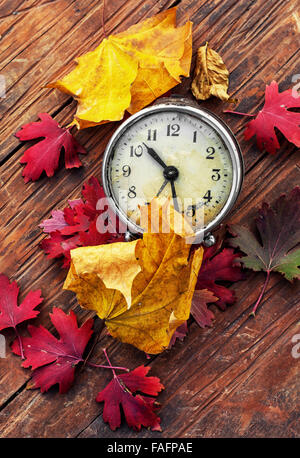 Obsolete alarm clock on wooden background strewn with fallen leaves Stock Photo