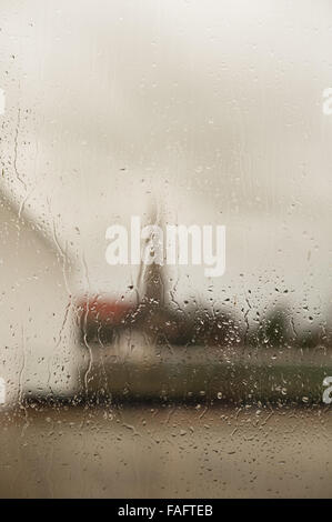 church and spire of church against skyline looking out from very wet rainy window with drops droplets running down glass pane Stock Photo