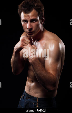 Portrait of muscular man with fighting stance against black background. Stock Photo