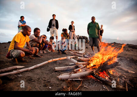 Tourists and local Nivans keep warm by a magma-started fire on Mt Yasur, an active volcano on Vanuatu's southern Tanna Island. Stock Photo